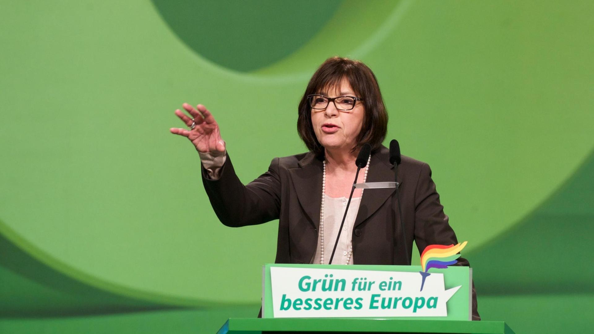 Grünen-Politikerin Rebecca Harms steht vor grünem Hintergund an einem ebenfalls grünen Rednerpult mit der Aufschrift: "Grün für ein besseres Europa". Sie spricht und gestikuliert, indem sie ihre rechte Hand hebt.