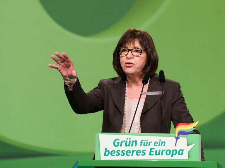 Grünen-Politikerin Rebecca Harms steht vor grünem Hintergund an einem ebenfalls grünen Rednerpult mit der Aufschrift: "Grün für ein besseres Europa". Sie spricht und gestikuliert, indem sie ihre rechte Hand hebt.