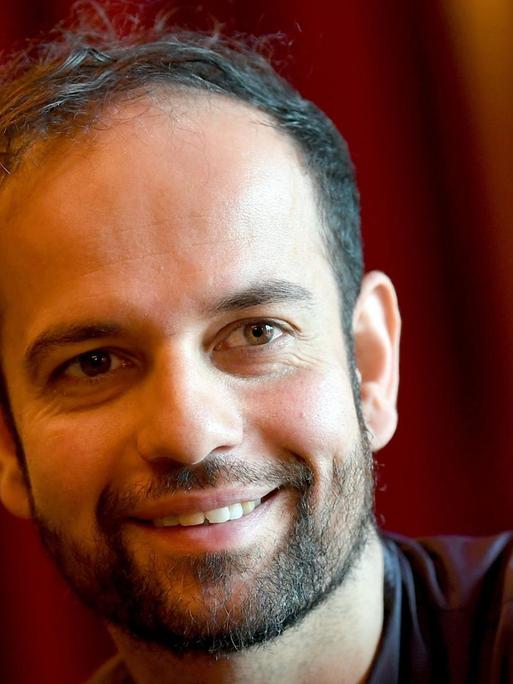 Der Künstler Tino Sehgal aufgenommen am 06.11.2017 in der Volksbühne in Berlin sitzt vor einem roten Vorhang