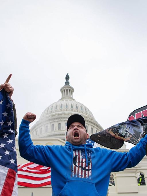 Ein Trump-Anhänger steht mit geballter Faust, offenem Mund und einer US-Fahne vor dem Kapitol in Washington.