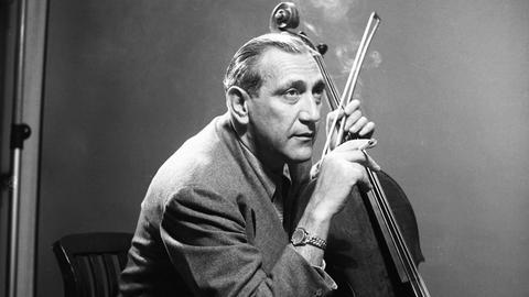 Der Cellist Gregor Piatigorsky im Anzug sitzend mit seinem Cello, in der linken Hand hält er den Bogen, in der rechten Hand eine Zigarette