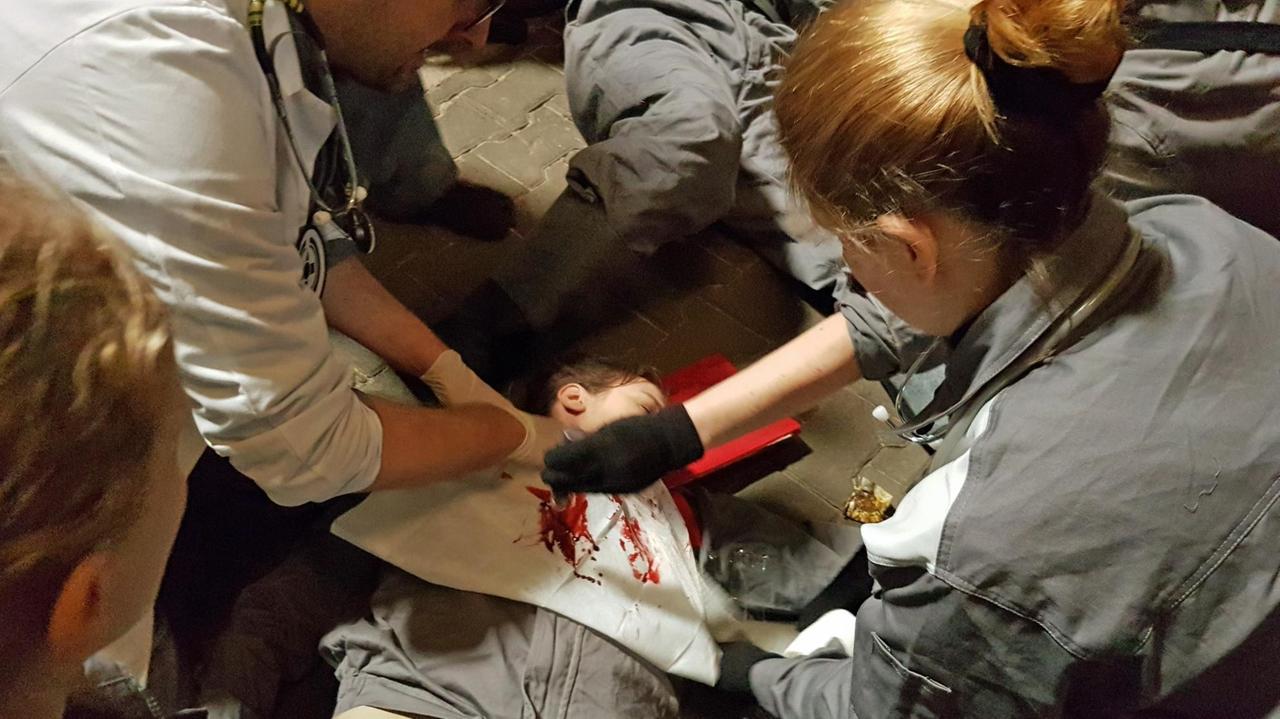 Menschen in grauer Uniform umringen einen blutenden Menschen, um ihm zu helfen.
