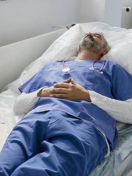 Ein erschöpfter Arzt liegt auf der Liege in einem Krankenhausflur und schläft.