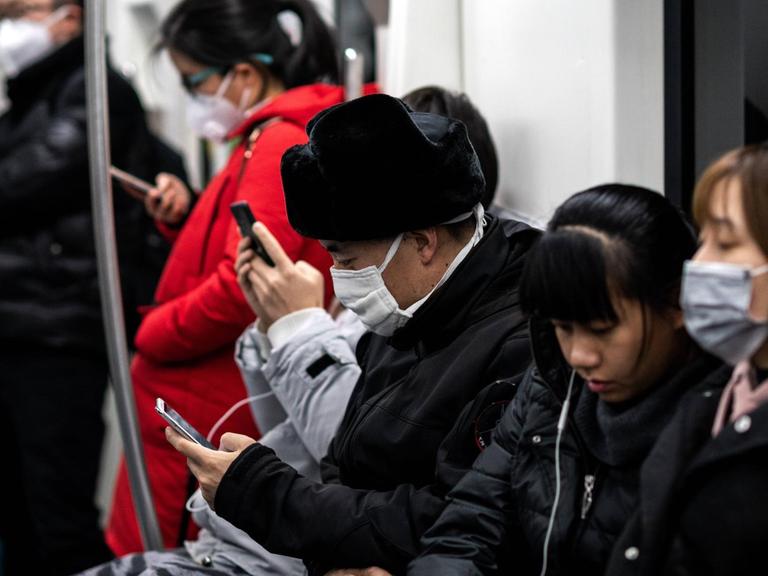 Menschen in einer U-Bahn in Peking. Sie tragen Mundschutz und schauen auf ihre Handys.