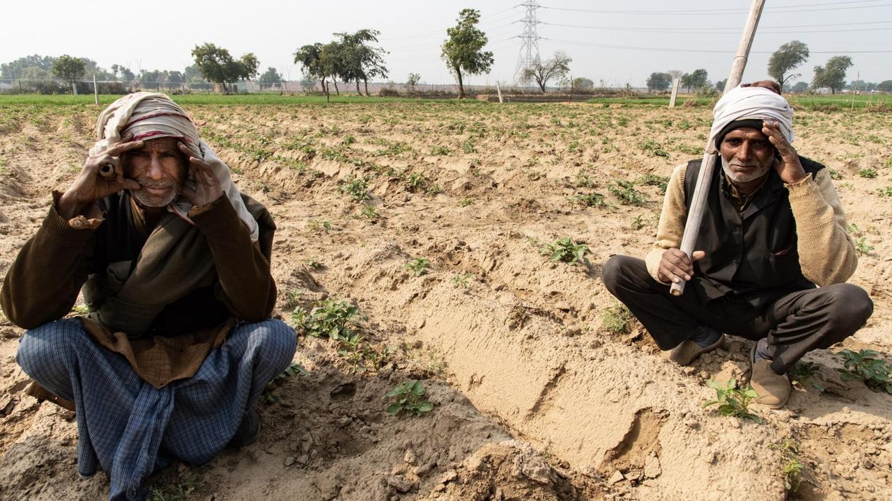 Bauer Chotlal Lhodal (links) und ein anderer Mann sitzen auf einem vertrockneten Feld