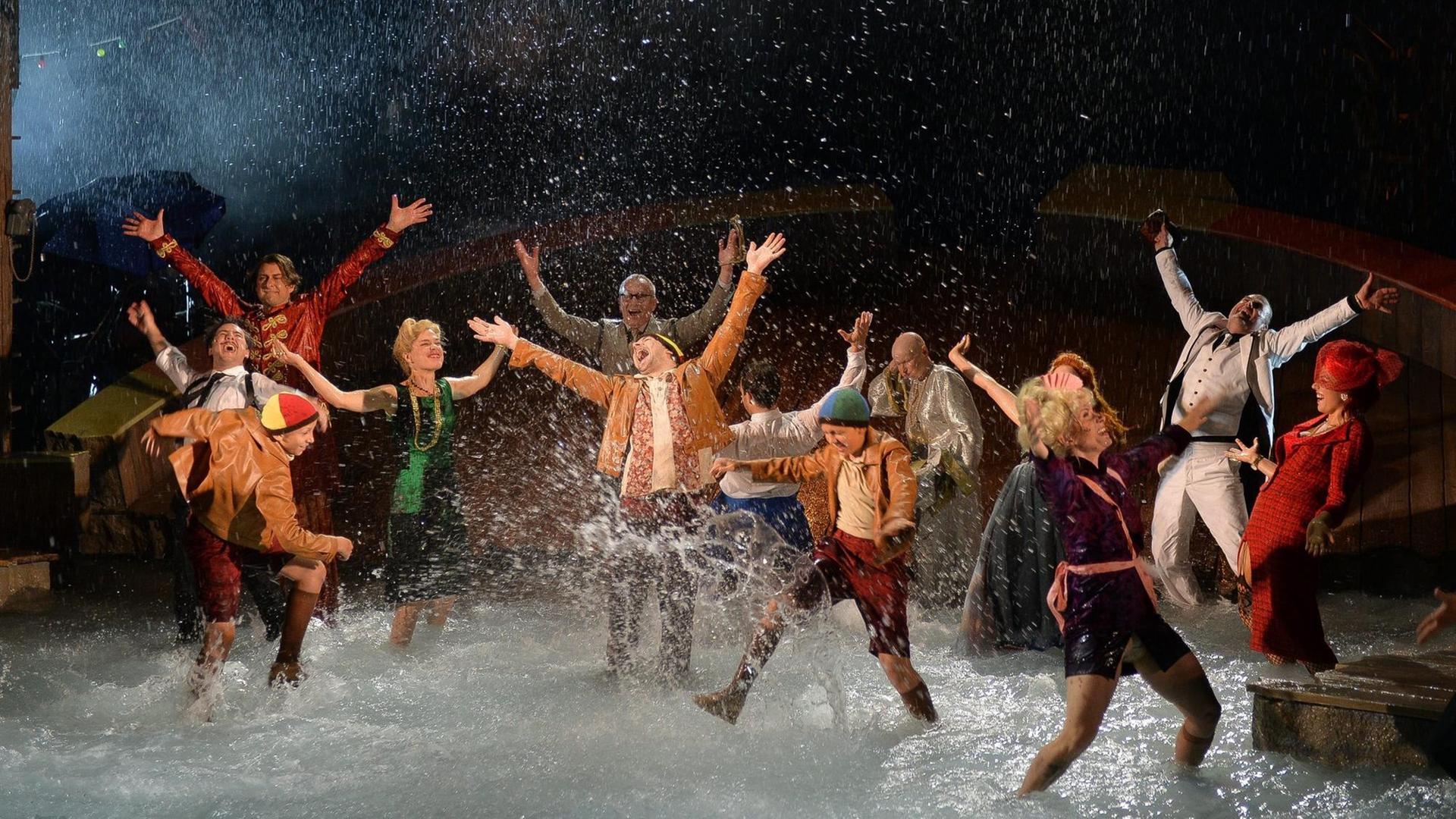 Schauspieler tanzen auf einer Bühne, deren Boden von Wasser bedeckt ist, Wasser spritzt in die Luft