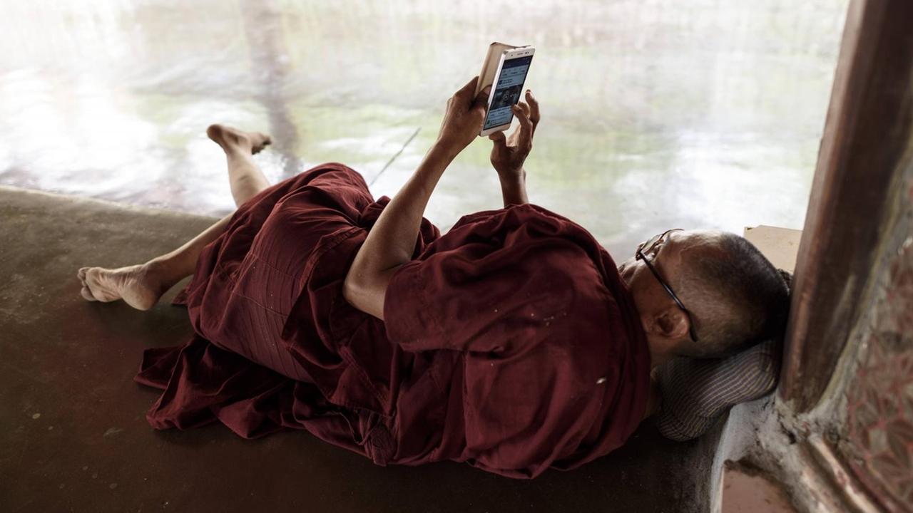 Ein buddhistischer Mönche besucht die Seite von Facebook auf seinem Samrtphone in der Kawhnat Pagode - Kor Nat, Myanmar, 2017