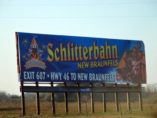 Großes blaues Schild am Straßenrand mit Aufschrift: Schlitterbahn New Braunfels, Exit 607, HWY 46 to New Braunfels Großes blaues Schild am Straßenrand mit Aufschrift: Schlitterbahn New Braunfels, Exit 607, HWY 46 to New Braunfels