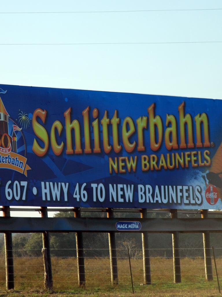 Großes blaues Schild am Straßenrand mit Aufschrift: Schlitterbahn New Braunfels, Exit 607, HWY 46 to New Braunfels Großes blaues Schild am Straßenrand mit Aufschrift: Schlitterbahn New Braunfels, Exit 607, HWY 46 to New Braunfels