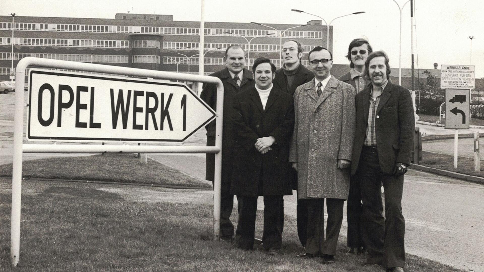 Das alte Foto zeigt sechs Vertreter der Arbeiterschaft von Opel Bochum vor dem Werksgebäude. Links im Bild weist ein Schild auf das Werk hin.
