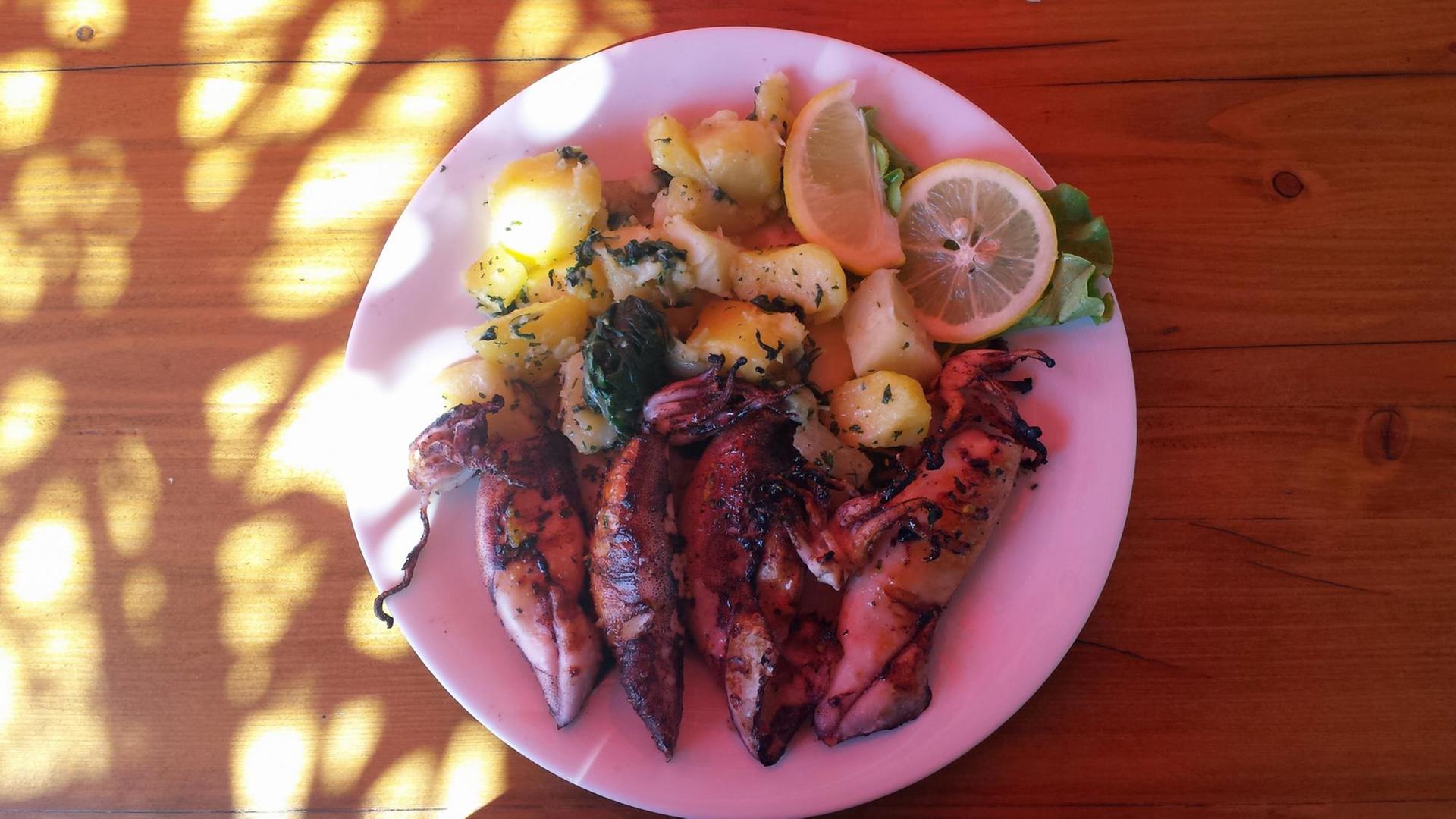 Gegrillter Tintenfisch liegt mit Kartoffeln und Spinat auf einem Teller.