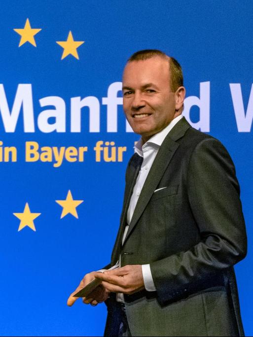 Weber geht lächelnd an einer blauen Wand mit dem europäischen Sternenkreis vorbei, auf der steht: "Manfred Weber - ein Bayer für Europa".
