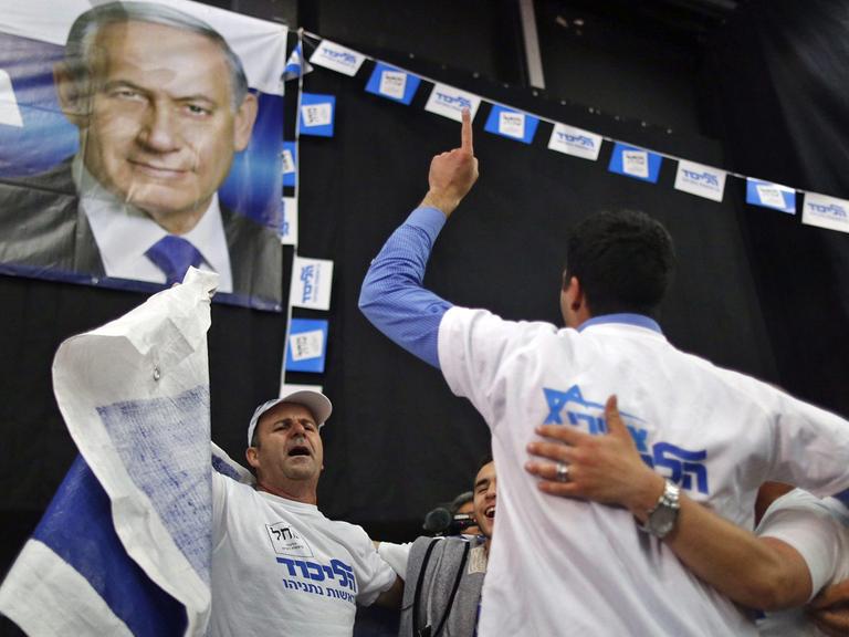 Männer mit Partei-T-Shirts bekleidet tanzen im Kreis unter einer Flagge mit dem Bild von Benjamin Netanjahu