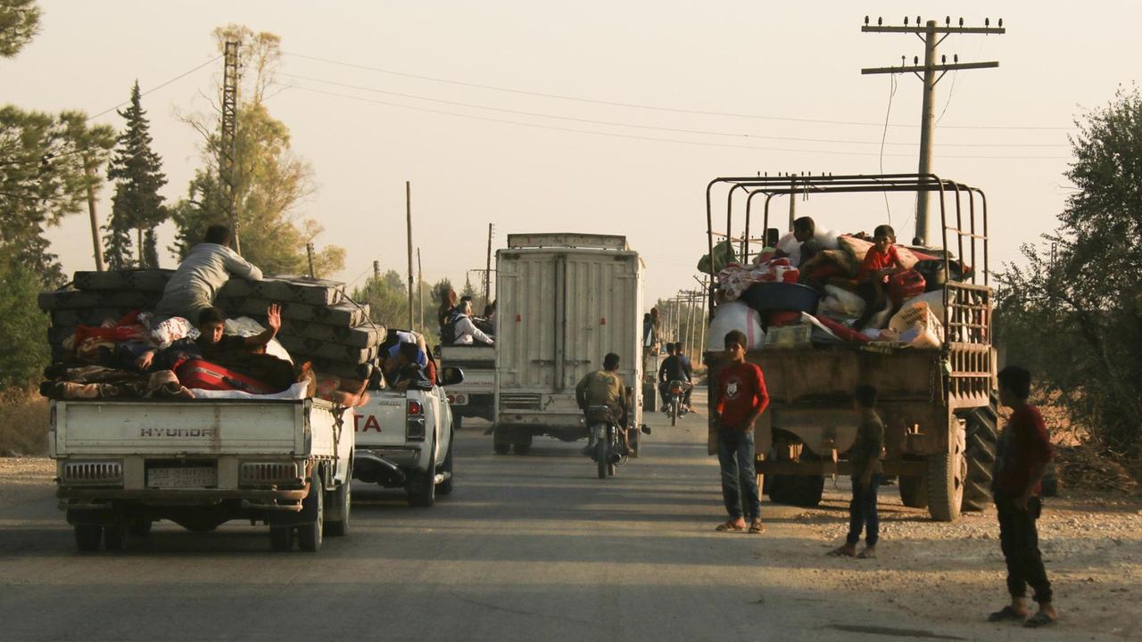 Syrer fliehen vor türkischen Truppen in Ras al Ayn, Nordostsyrien. Mehrere offene Lastwagen mit Menschen auf der Ladefläche. 