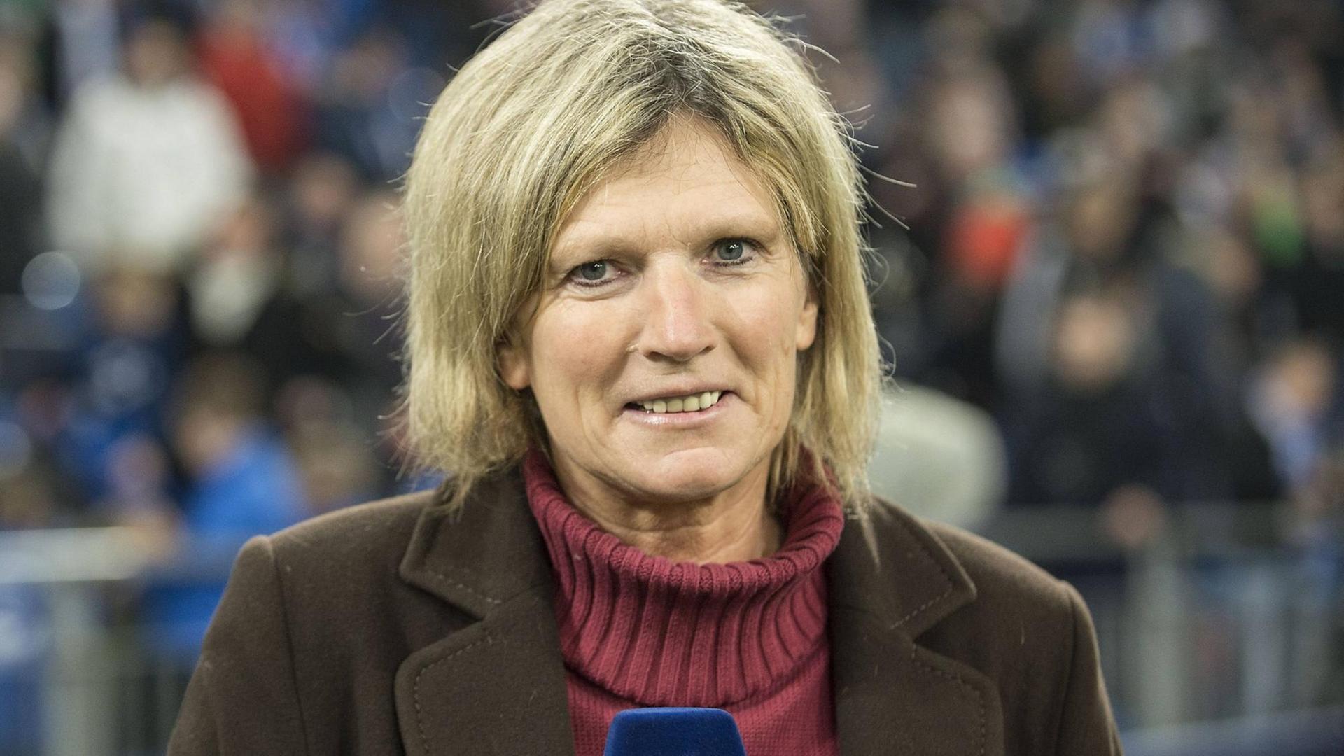 Claudia Neumann mit einem ZDF-Mikrophon in der Hand in einem Fußballstadion.