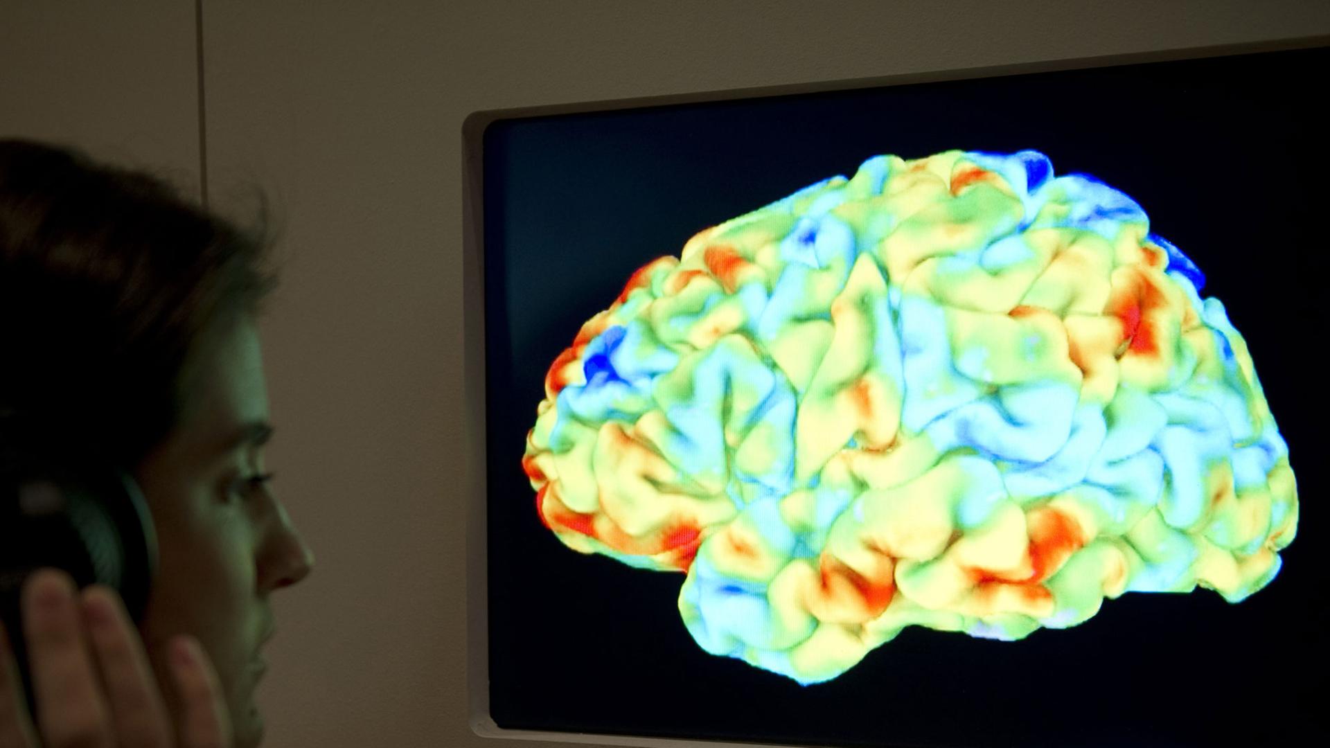 Eine Frau betrachtet eine Magnetresonanztomographie-Aufnahme (MRT) eines menschlichen Gehirns.