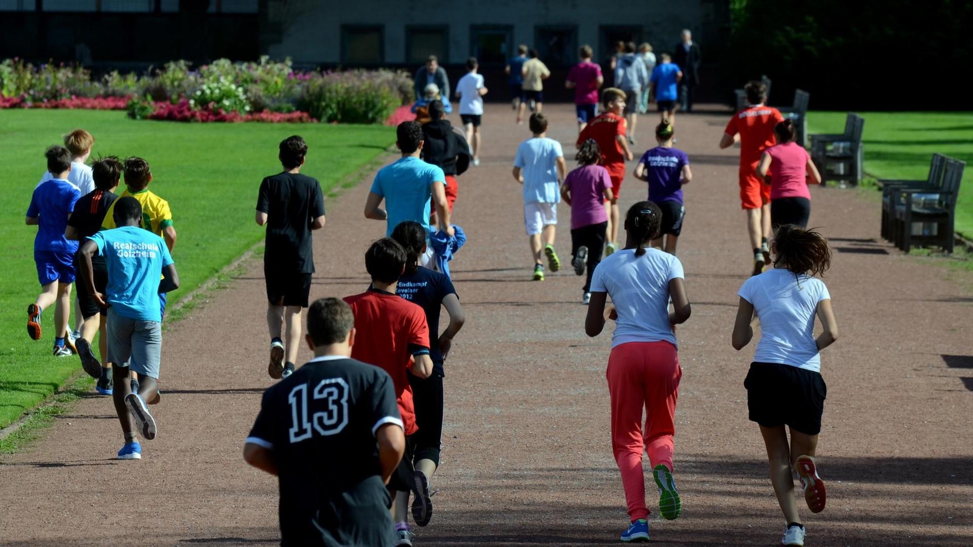Schüler- und Schülerinnen laufen in Düsseldorf beim Schulsport durch eine Parkanlage.