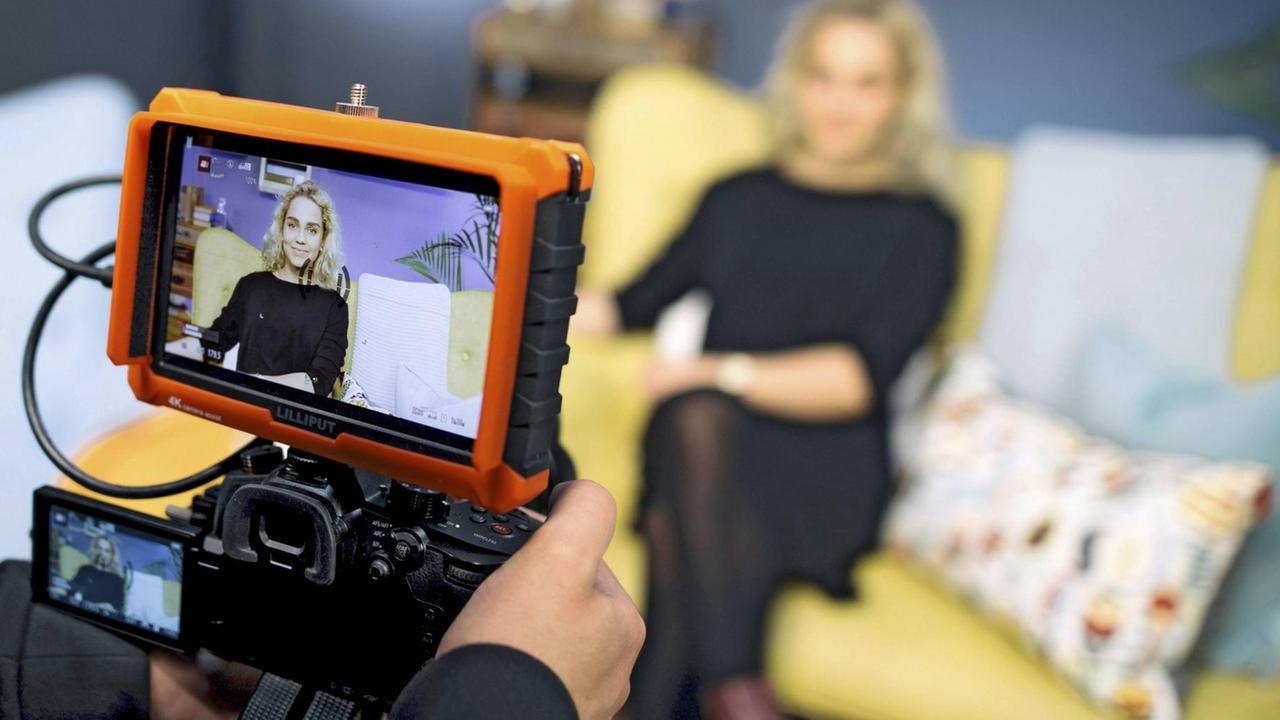 Die Youtuberin Jana Highholder sitzt auf einem gelben Sofa und wird von einer Kamera gefilmt.