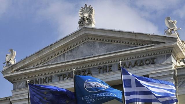 Vor dem Gebäude der griechischen Nationalbank in Athen flattern Flaggen der EU, der Bank und Griechenlands im Wind.