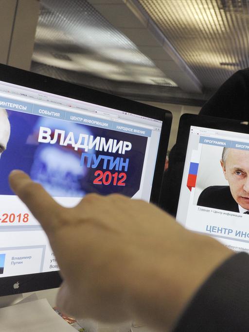 Ein Finger zeigt auf zwei Computerbildschirme, auf denen der russische Präsident Wladimir Putin zu sehen ist.
