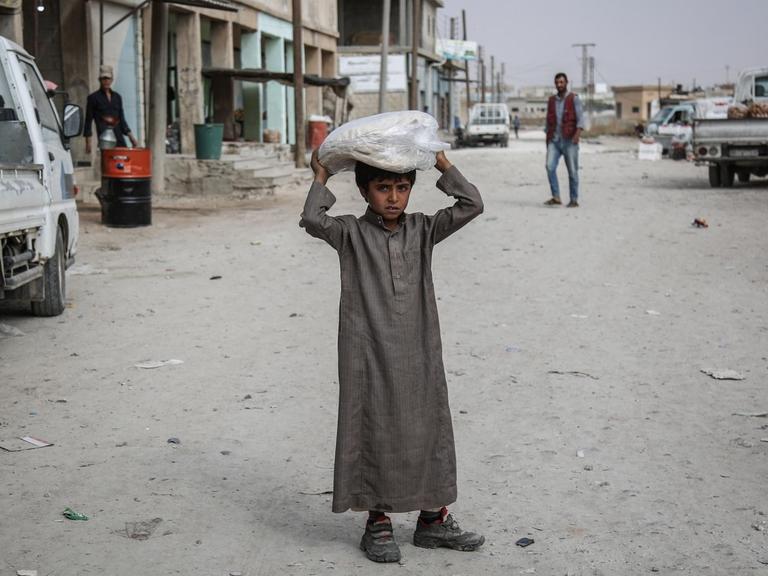 Ein syrischer Junge trägt auf einer Straße Essen auf seinem Kopf.