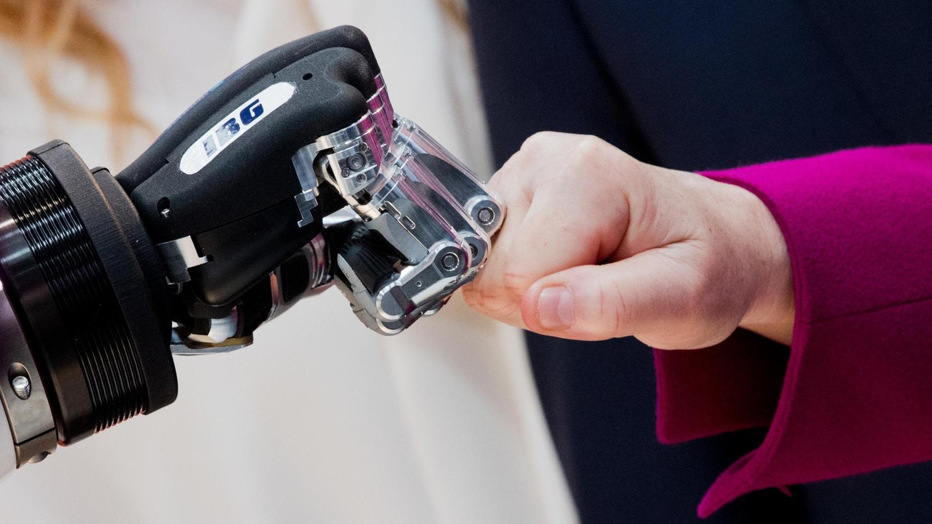 Die Hände von Bundeskanzlerin Merkel und einem Roboter berühren sich