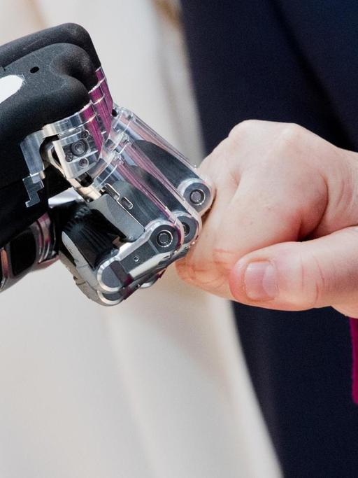 Die Hände von Bundeskanzlerin Merkel und einem Roboter berühren sich