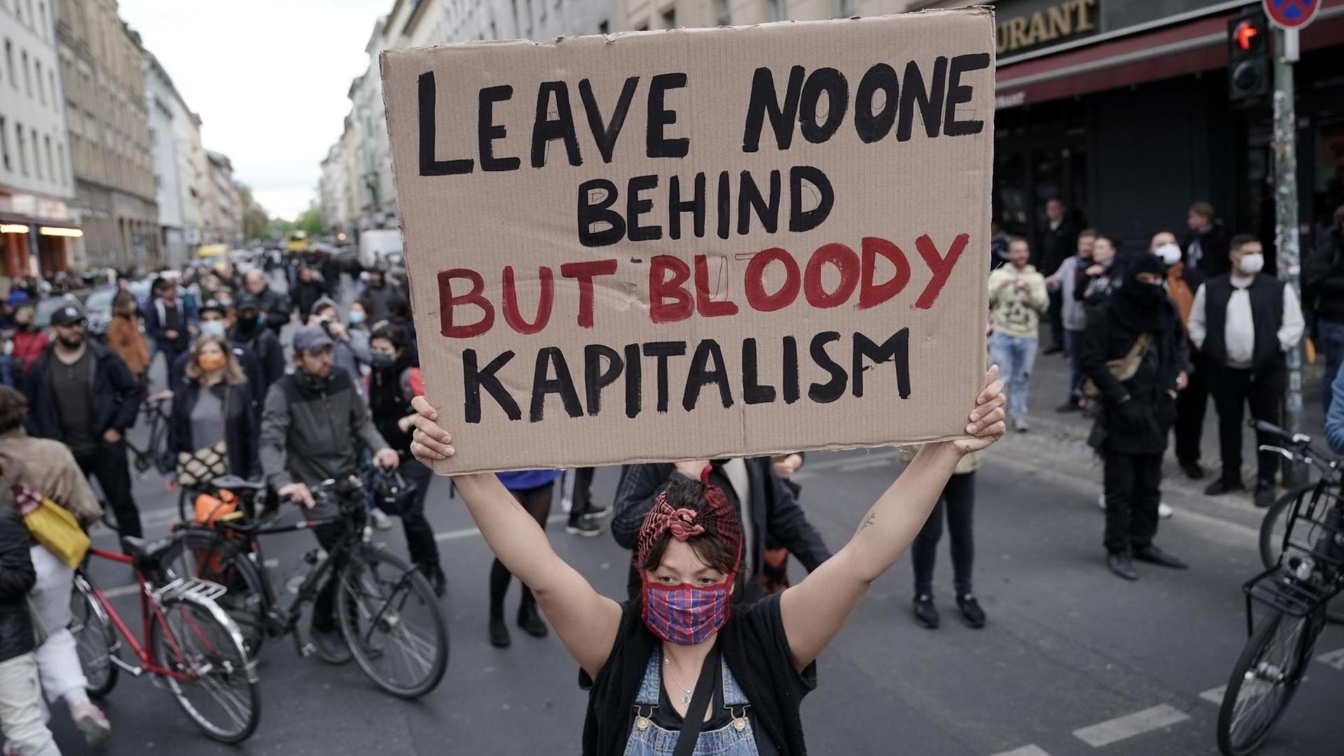 Eine Demonstrantin hält ein Plakat mit der Aufschrift "Leave no one behind but bloody kapitalism" auf der Oranienstraße in Kreuzberg hoch