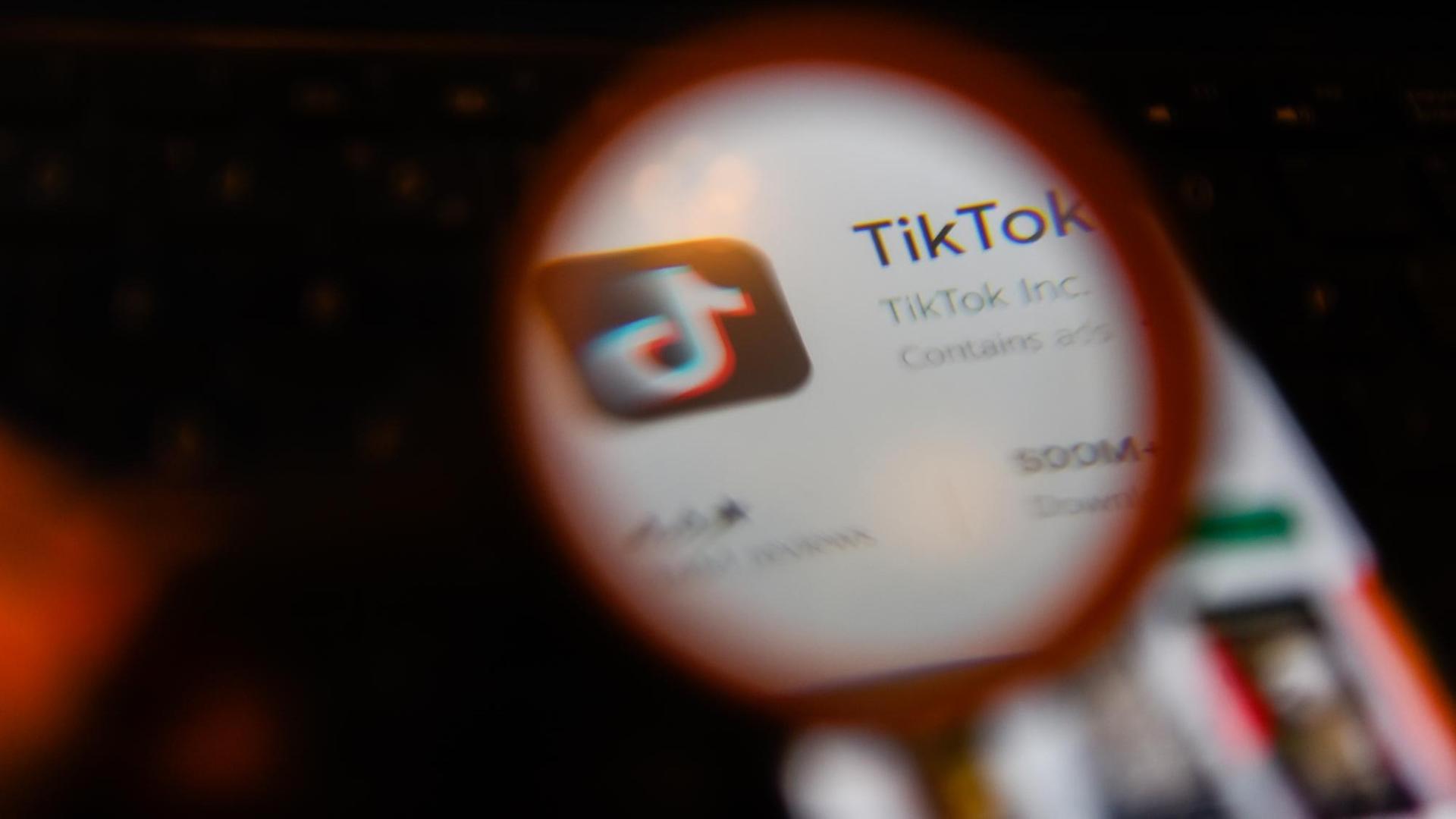 Die App Tik Tok auf einem Smartphonebildschirm durch eine Lupe gesehen.