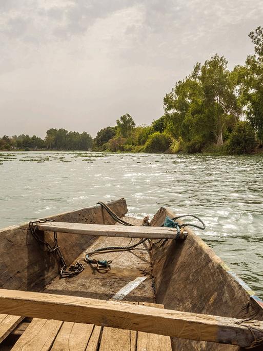 Im Hinterland, wo einmal die Geheime Stadt gestanden hat, wohnt Bowguard. Zu sehen: Die Spitze eines alten Holzboots auf dem Niger. Am Ufer sind Bäume und eine Graslandschaft.