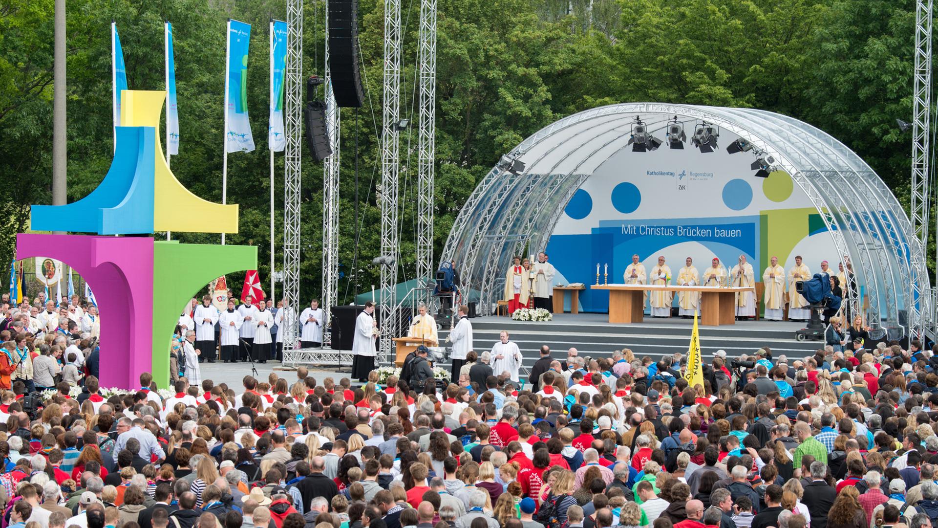 Zahlreiche Gläubige nehmen am 01.06.2014 in Regensburg (Bayern) am Abschlussgottesdienst des Katholikentages teil. Sie stehen vor einer Bühne, in deren Nähe ein großes buntes Kreuz aufgebaut ist. Zahlreiche Gläubige nehmen am 01.06.2014 in Regensburg (Bayern) am Abschlussgottesdienst des Katholikentages teil. Sie stehen vor einer Bühne, in deren Nähe ein großes buntes Kreuz aufgebaut ist.