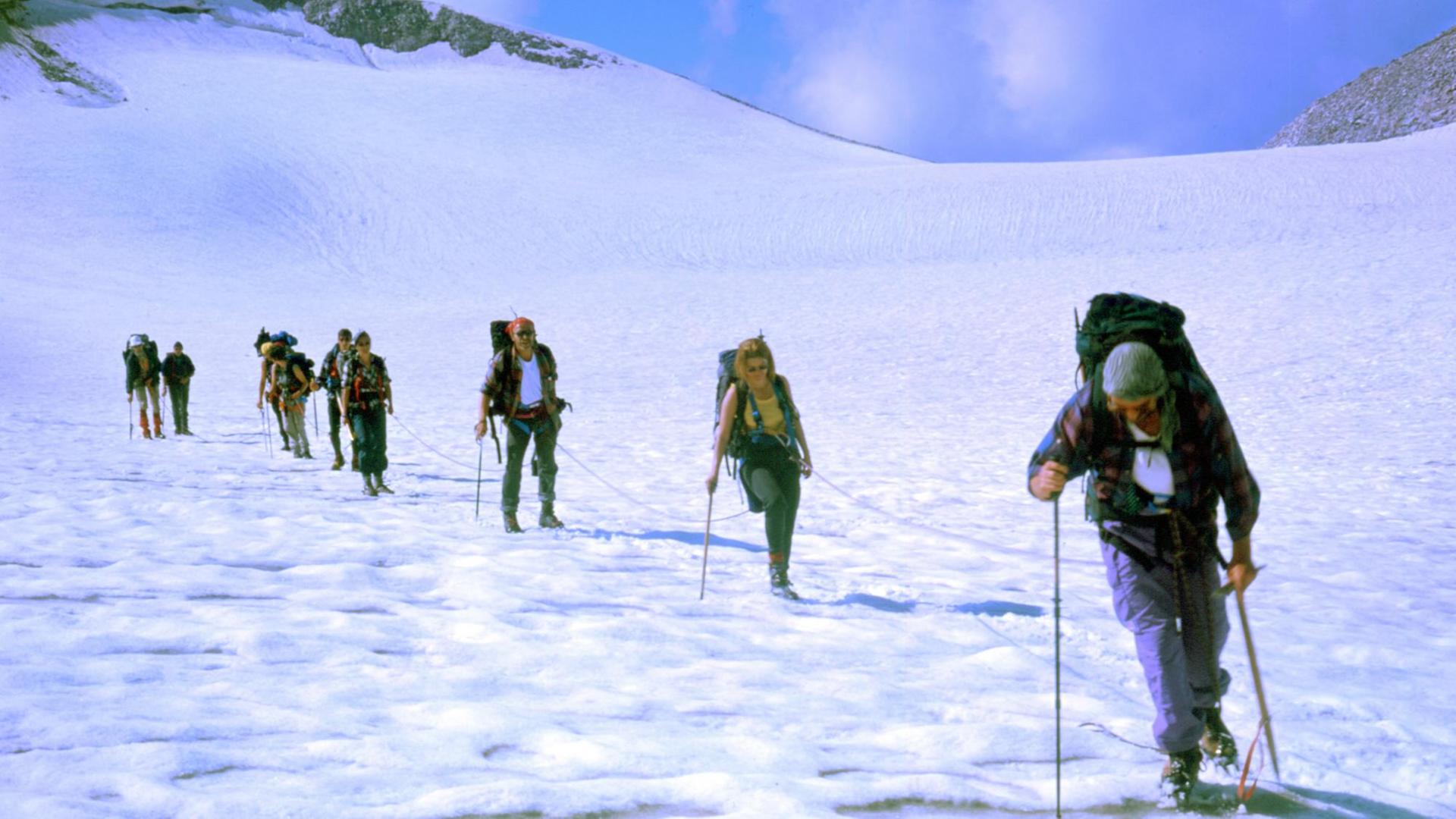 Mehrere Bergsteiger gehen in einer Reihe über eine schneebedeckte Landschaft