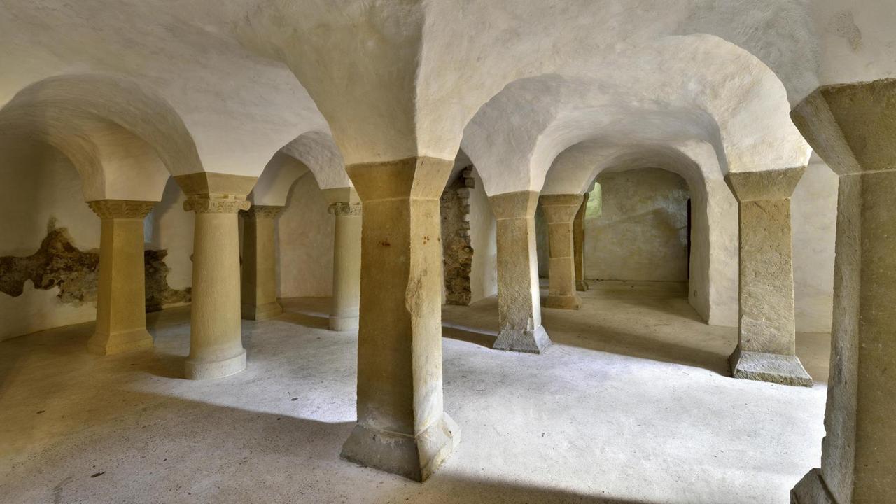 Blick hindurch zwischen Säulen einer unterirdischen Krypta. Die Decke wird von einem Gewölbe gehalten.