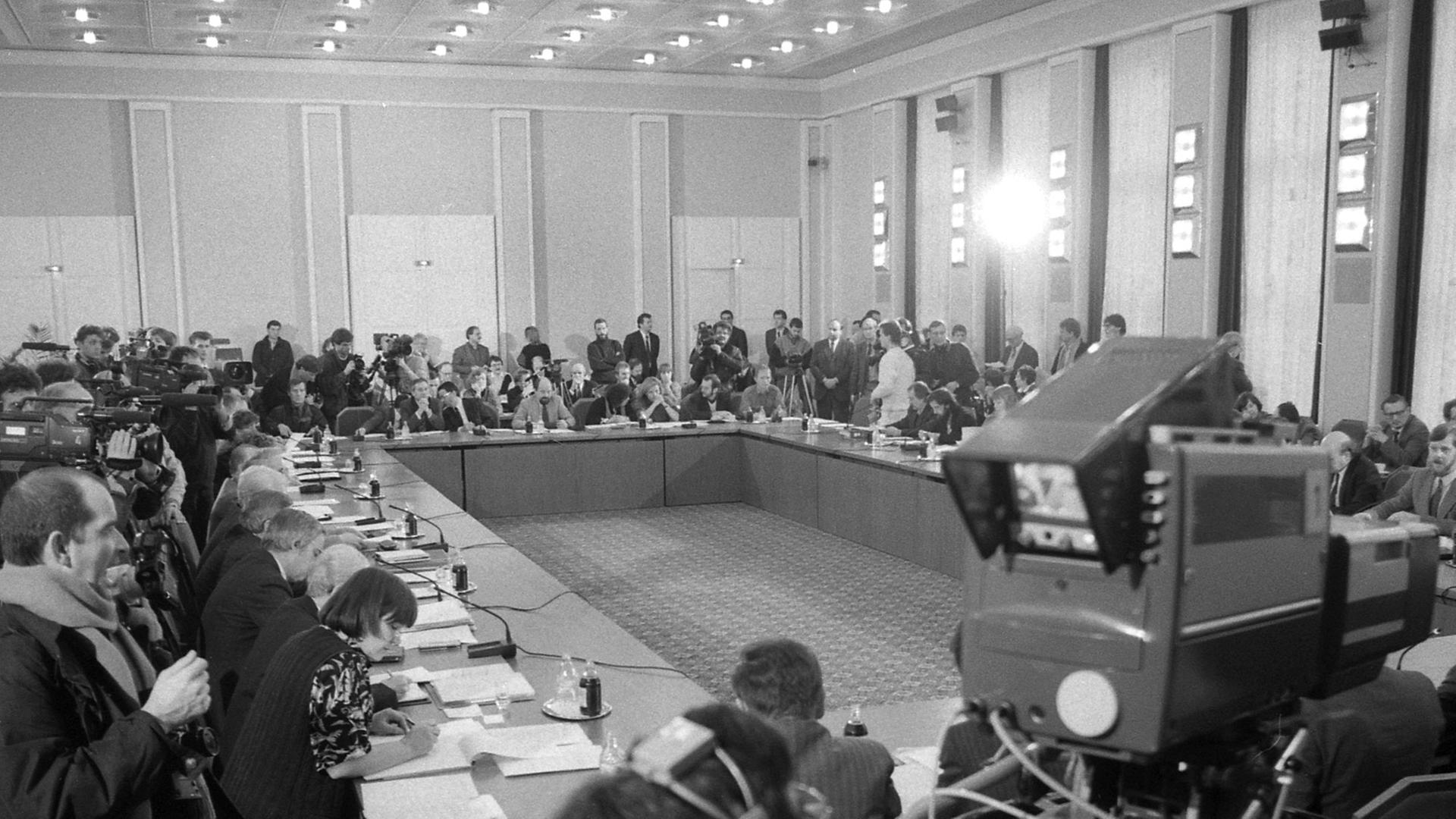 Versammlung im Januar 1990 am Zentralen Runden Tisch im Konferenzgebäude des Ministerrates der DDR am Schloss Niederschönhausen (heute Schönhausen) in Berlin-Pankow. In der Wendezeit war mit dem Wegbrechen hierarchischer Strukturen ein Machtvakuum in der DDR entstanden. Der Zentrale Runde Tisch, an dem Vertreter von Parteien, der Kirche, gesellschaftlichen Institutionen und der neuen Bürgerbewegung mitarbeiteten, beeinflusste viele Entscheidungen der Übergangsregierung Modrow und erfuhr wegen seiner Bedeutung für das Land ein großes Medieninteresse.