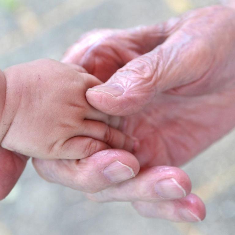 Eine Babyhand liegt in der Hand eines alten Menschen.