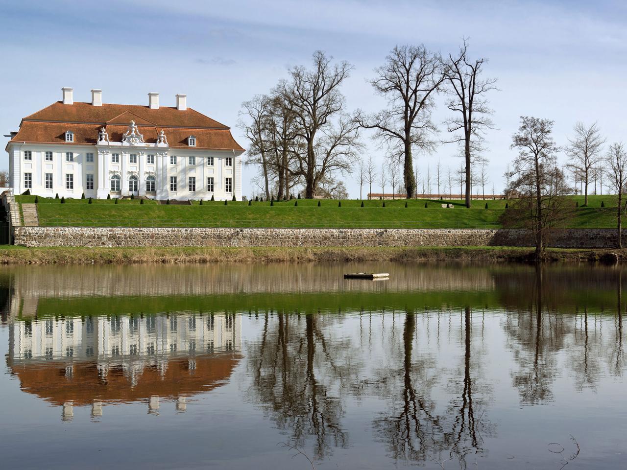 Das Gästehaus der Bundesregierung, Schloss Meseberg nördlich von Berlin in Brandenburg, spiegelt sich bei strahlendem Sonnenschein im Huwenowsee.