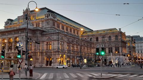 Die Wiender Staatsoper von außen fotografiert. Zu sehen sind ausserdem eine Kreutzung und einige Fußgänger*innen.