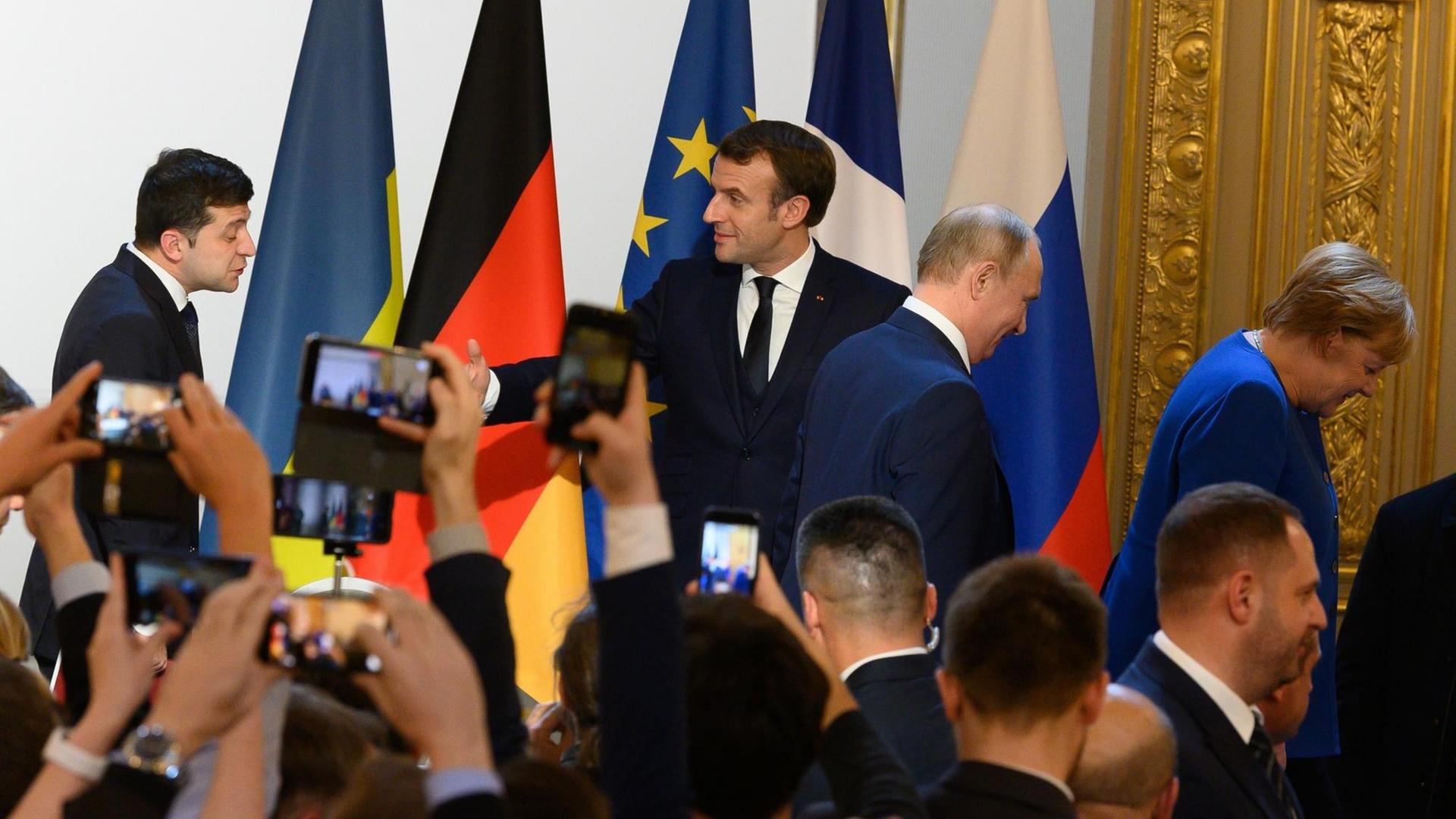 Smartphones werden in die Höhe gestreckt, um Wolodymyr Selenskyj, Emmanuel Macron, Wladimir Putin und Angela Merkel zu fotografieren.