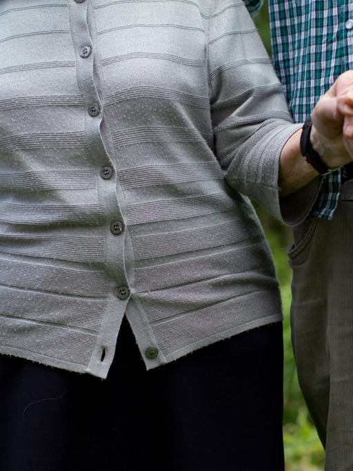Ein junger Mann geht mit einer Seniorin im Park spazieren.