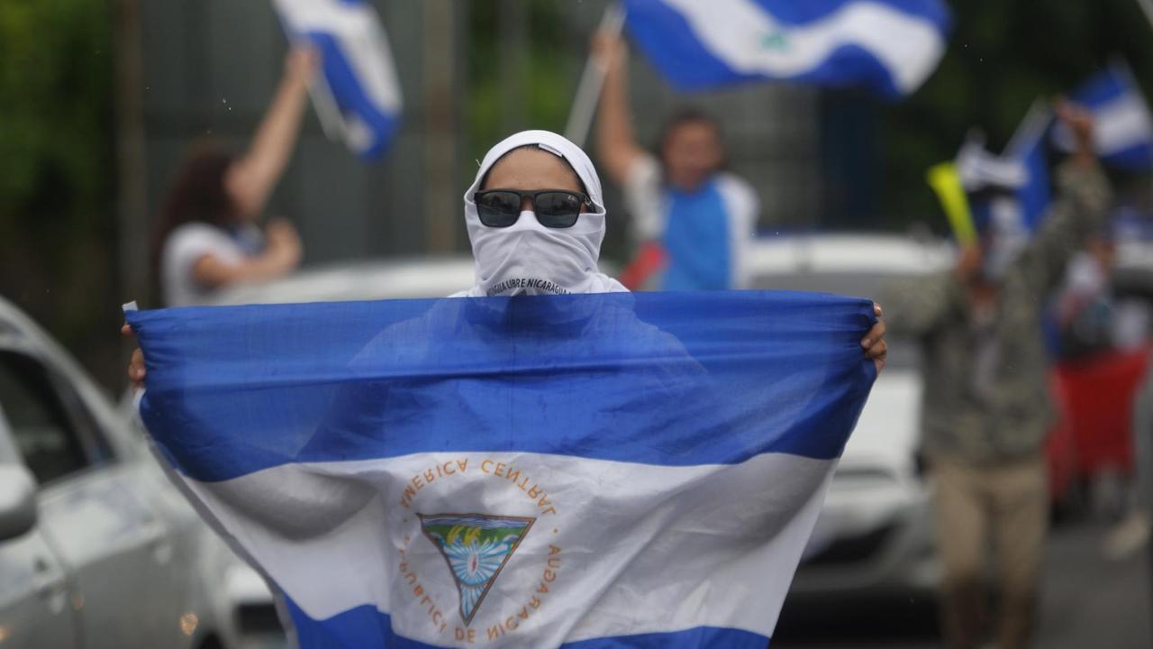 Proteste gegen Präsident Ortega in der Stadt Ticuantepe: Eine Demonstrantin läuft mit nicaraguanischer Nationalfahne zwischen Autos entlang