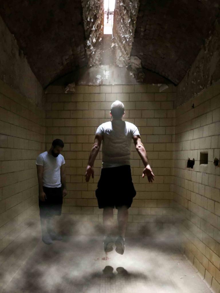 Zwei Menschen stecken in einem unterirdischen Trakt fest, einer von beiden springt nach oben, um näher an eine Luke in der Decke zu kommen, durch die Licht hineindringt.