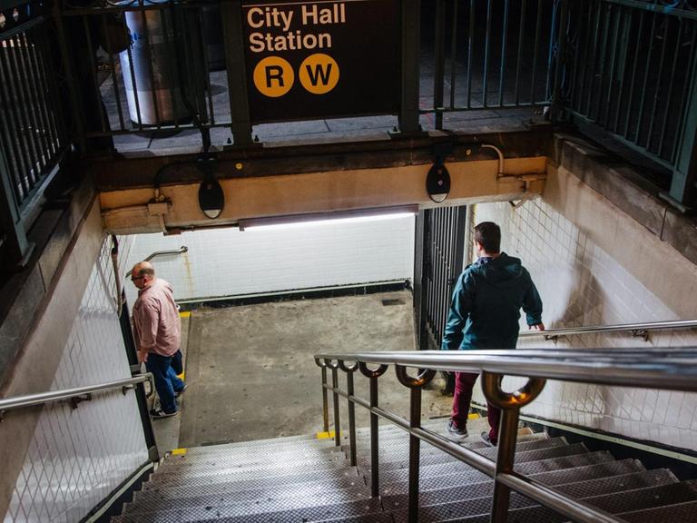 Eine U-Bahn-Station in Manhattan, Menschen gehen die Treppe zum Gleis hinunter.