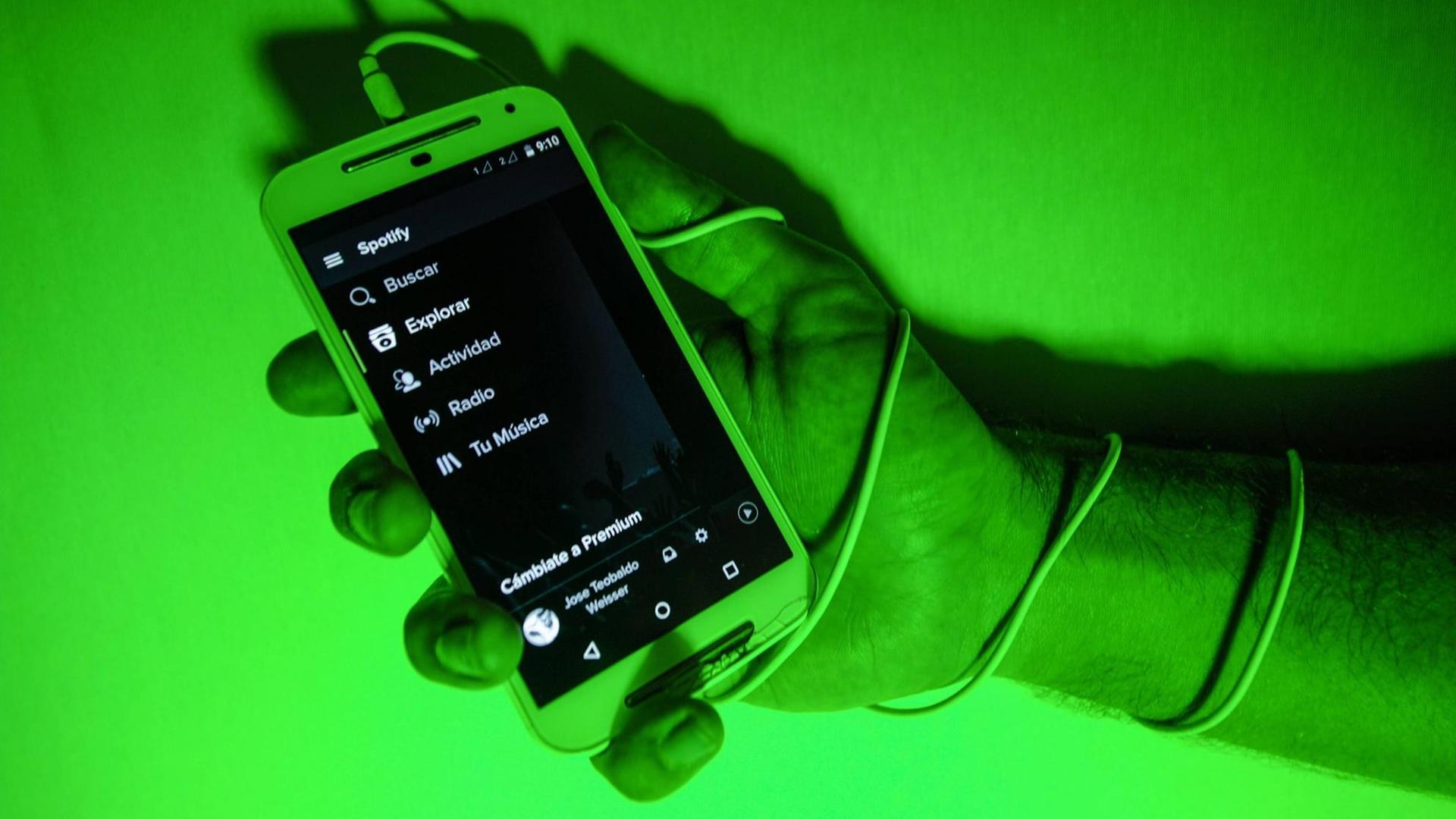 Hand hält Mobiltelefon, die Szene ist in grünes Licht getaucht.