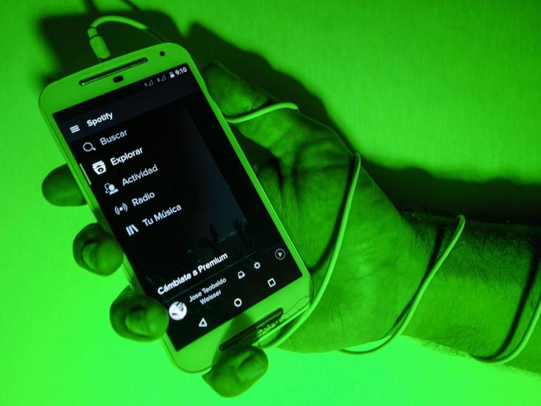 Hand hält Mobiltelefon, die Szene ist in grünes Licht getaucht.