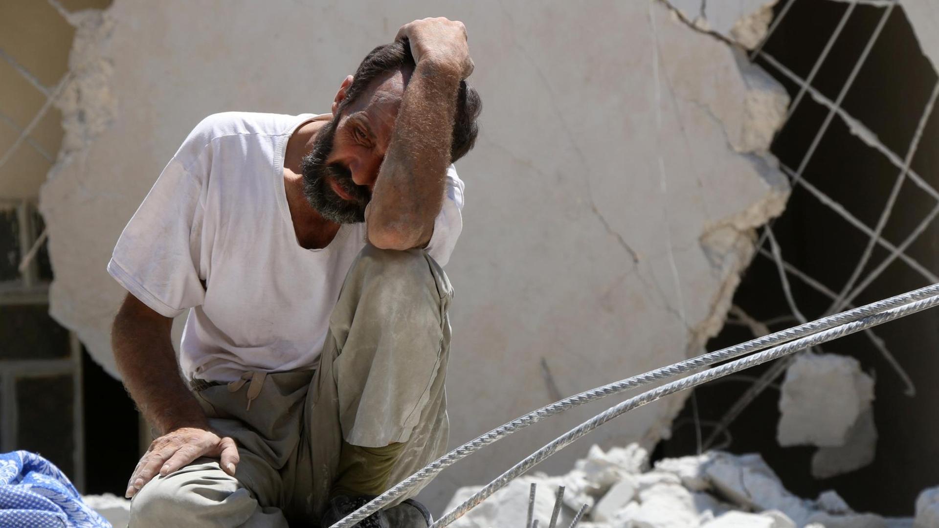 Ein Mann hält sich die Hand vor das Gesicht, er sitzt auf Trümmern. Das Foto entstand nach einem Bombenangriff in den Rebellenvierteln von Aleppo.