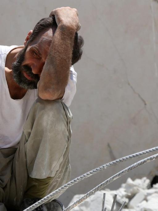 Ein Mann hält sich die Hand vor das Gesicht, er sitzt auf Trümmern. Das Foto entstand nach einem Bombenangriff in den Rebellenvierteln von Aleppo.