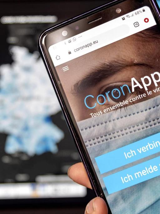 Die Freiwilige Corona-App app.coronapp.eu läuft auf einem Smartphone, im Hintergrund ist die Website des Robert Koch Instituts zu sehen.
