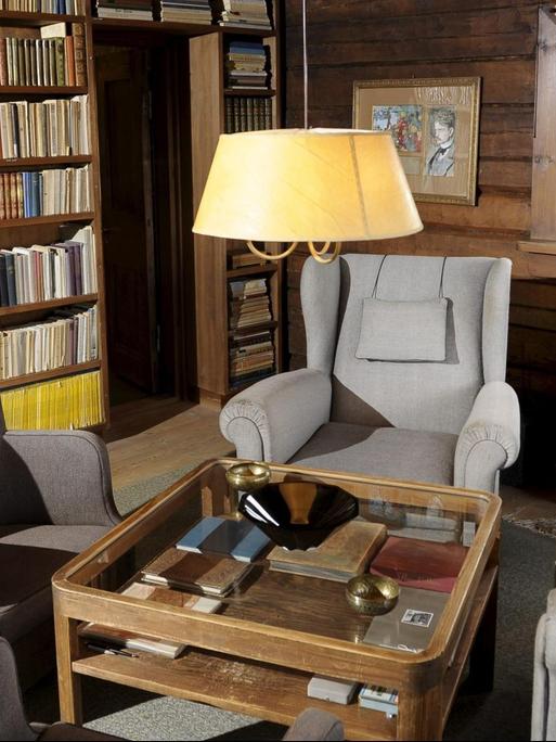 Eine gemütliche graue Sesselkombination steht um einen quadratischen Tisch vor einer deckenhohen Bücherwand.
