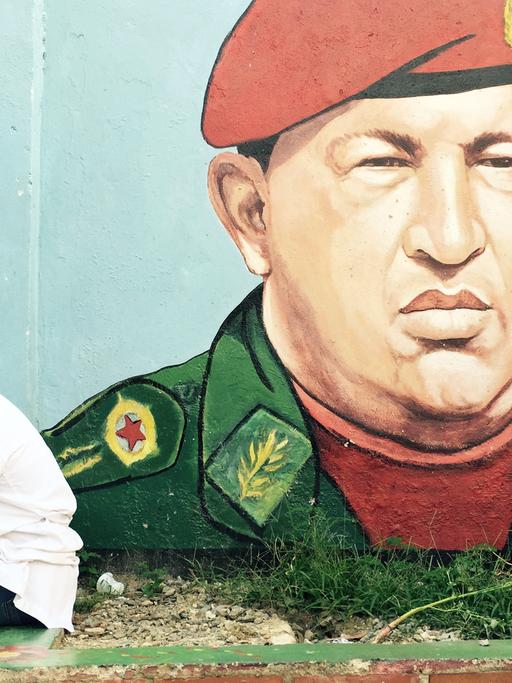 Ein junger Mann sitzt vor einem Graffiti von Hugo Chávez