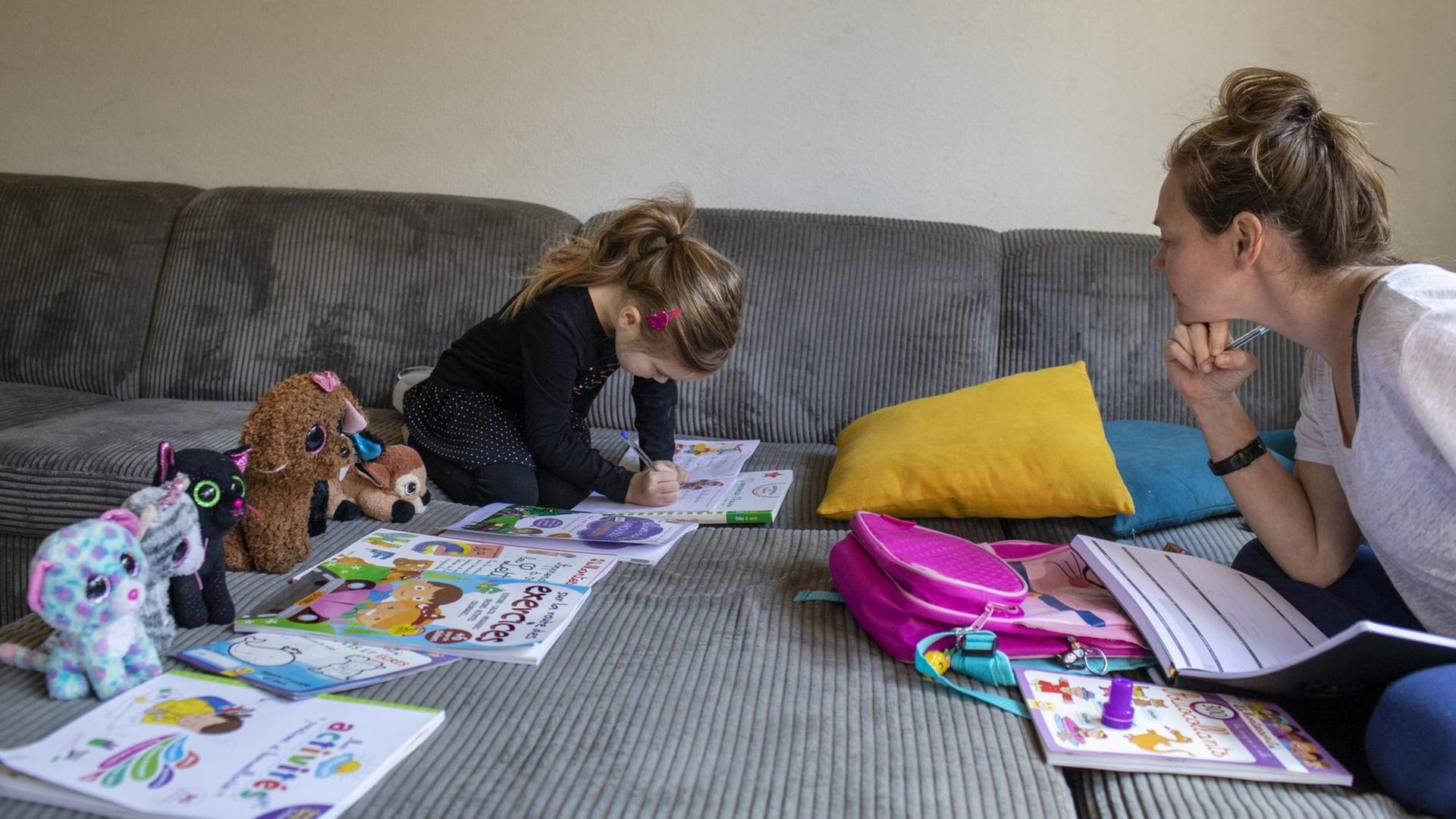 Abby, 6, mit ihrer Mutter Lisa beim Homeschooling auf dem Sofa zu Hause. Die Kuscheltiere sitzen auch alle vor einem Arbeitsheft. 20. März 2020 in Claira, Frankreich.